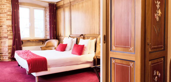 Chambre d’hôtel avec grand lit double, boiseries murales et espace salon attenant.