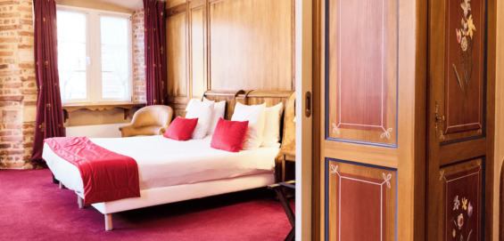 Chambre d’hôtel avec grand lit double, boiseries murales et espace salon attenant.